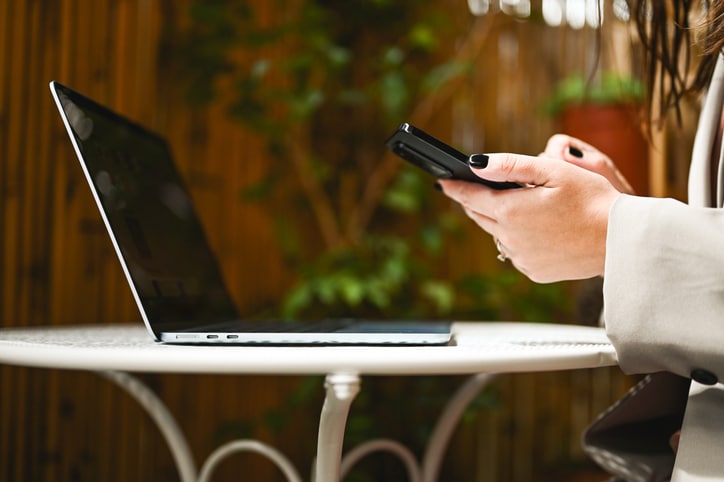 Financial Services professional using a smartphone beside an open laptop, representing business text messaging and client communications for financial advisory firms.