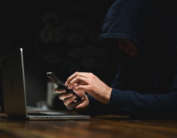 Person using a smartphone beside a laptop in a dark setting, representing Shadow AI and cybersecurity risks for RIAs.