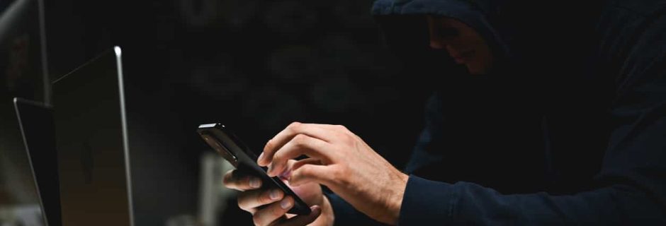 Person using a smartphone beside a laptop in a dark setting, representing Shadow AI and cybersecurity risks for RIAs.