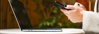 Financial Services professional using a smartphone beside an open laptop, representing business text messaging and client communications for financial advisory firms.