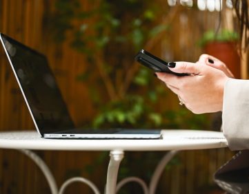 Financial Services professional using a smartphone beside an open laptop, representing business text messaging and client communications for financial advisory firms.